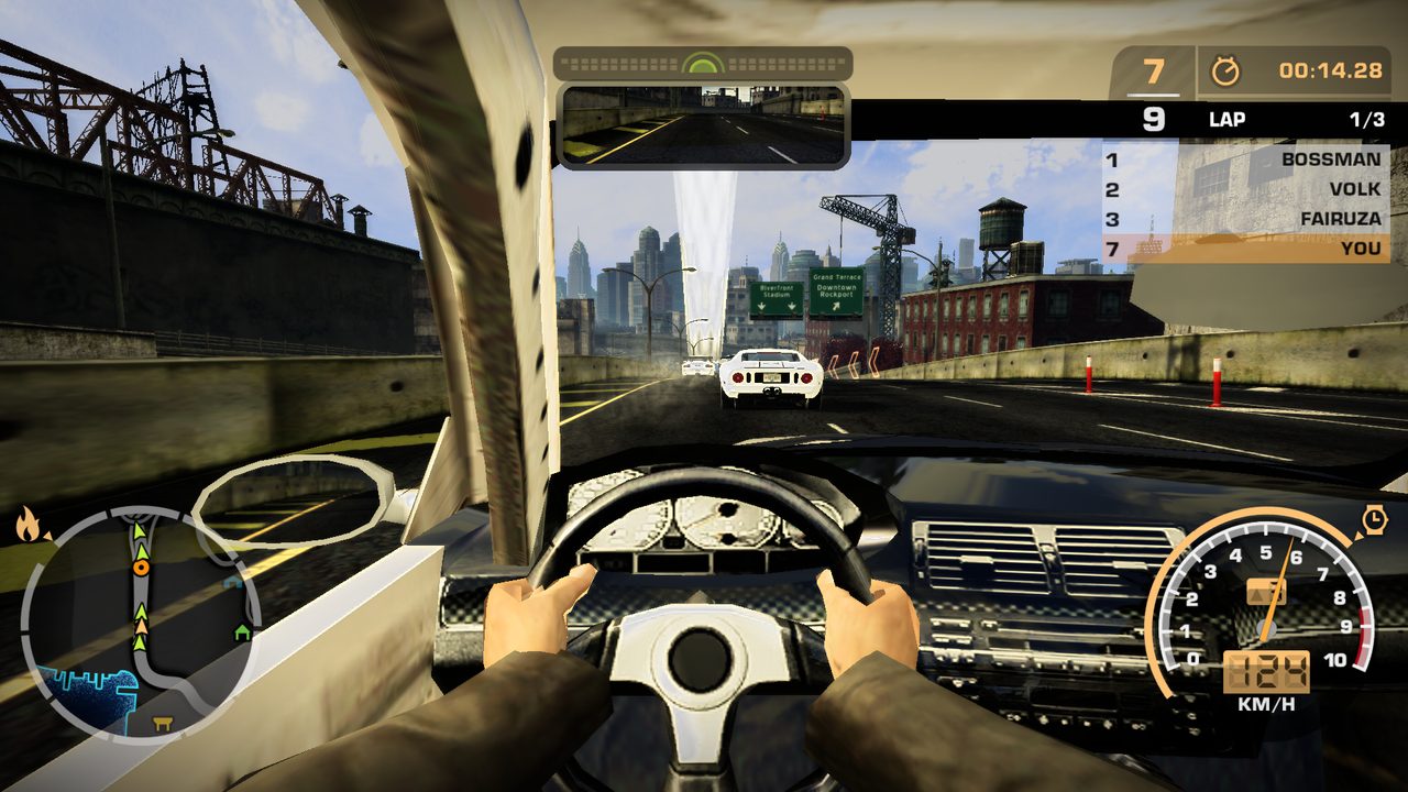 First-person view from inside a car on a Rockport highway: the driver's hands in brown jacket sleeves on a three-spoke steering wheel, a rear-view mirror at the top showing the road behind, a side mirror at left, the race HUD with lap 1 of 3 and position 7 of 9, a speedometer reading 124 km/h, and a white Ford GT ahead.
